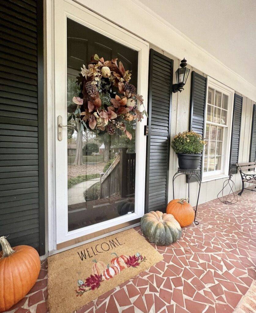 A black door with a fall wreath and pumpkins.