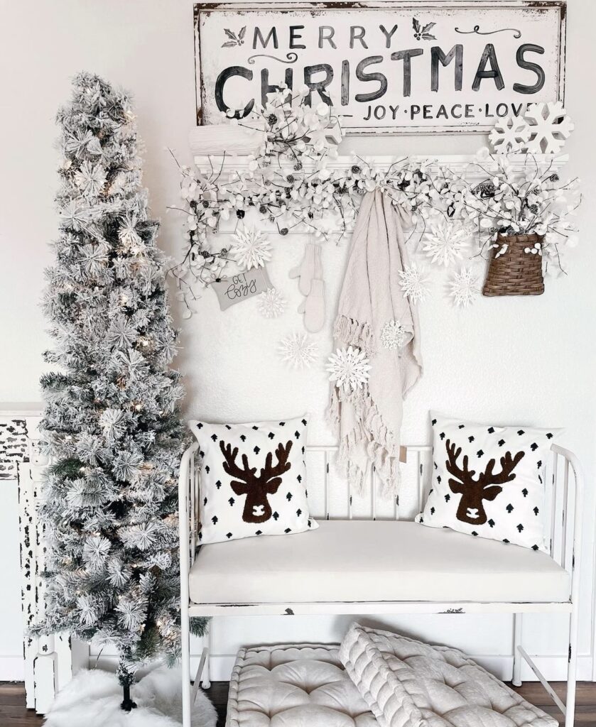 A white bench with white pillows and a white wooden Christmas sign.