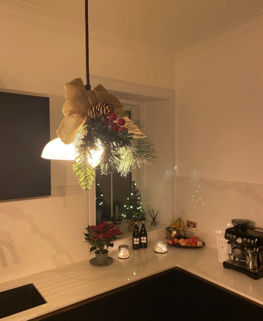 A light fixture decorated with pine branches, pine cones and red berries.