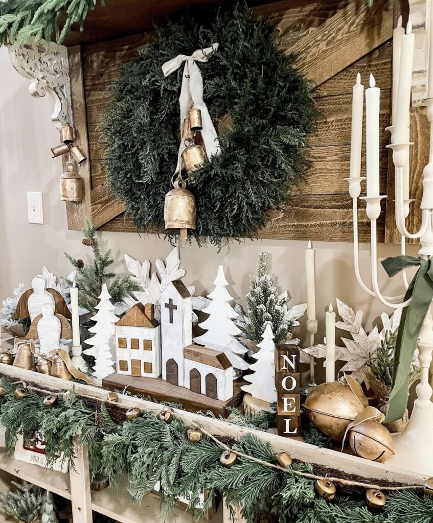 A wreath with bells above a wooden Christmas willage.