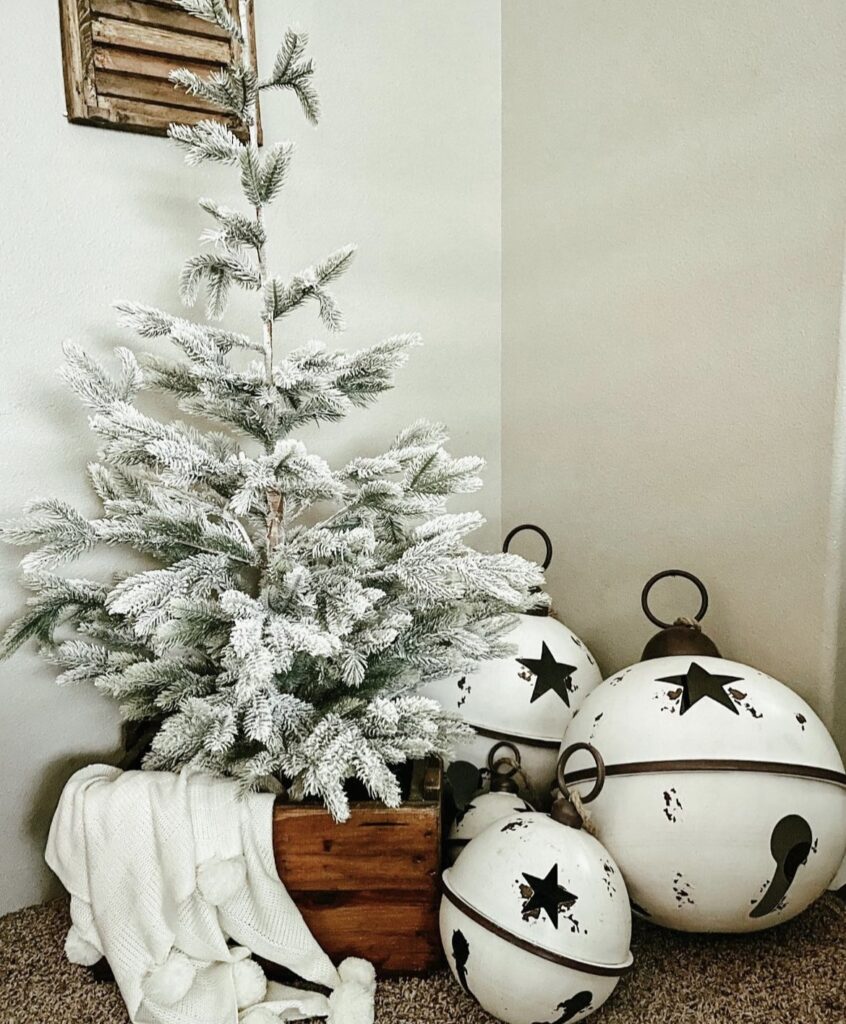 A white Christmas tree next to large white jingle bells.