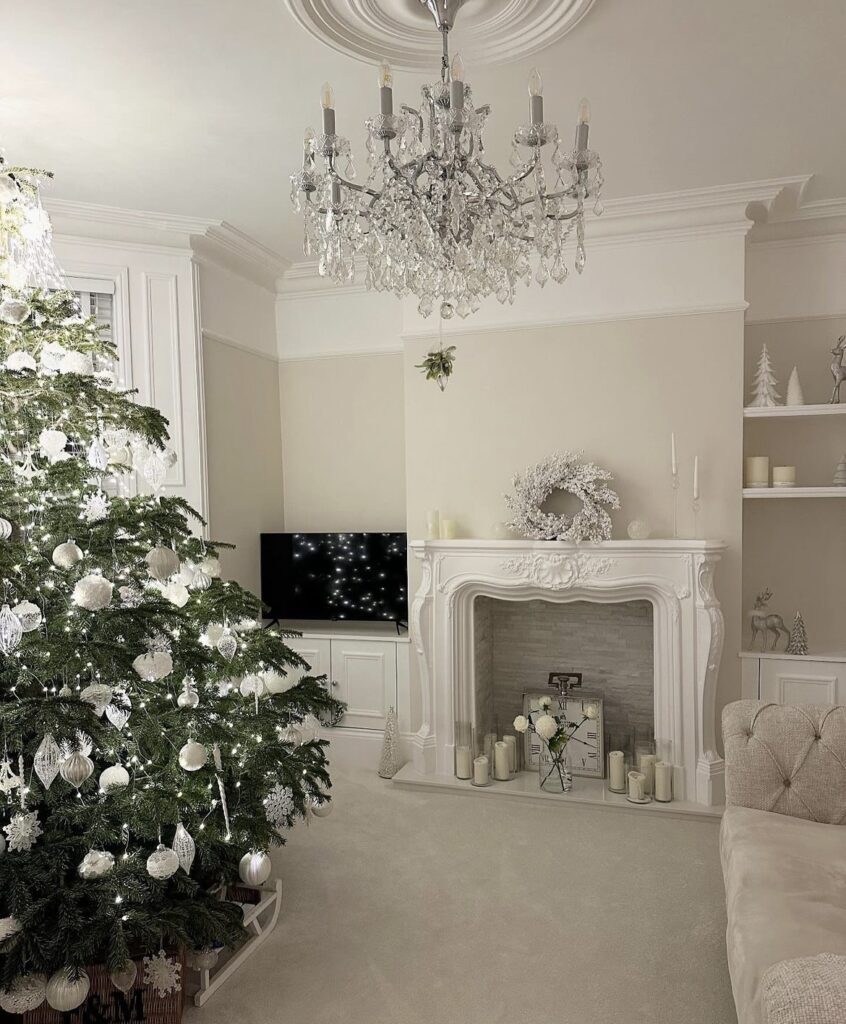 A white mantel with a white Christmas wreath and white candles.