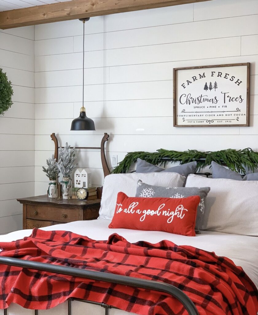 A bed with red bedding and a Christmas sign above it.