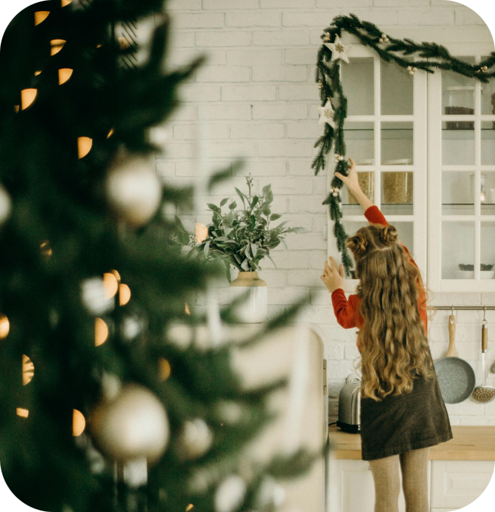 A child placing a pine garland on top of a kitchen cabinet.