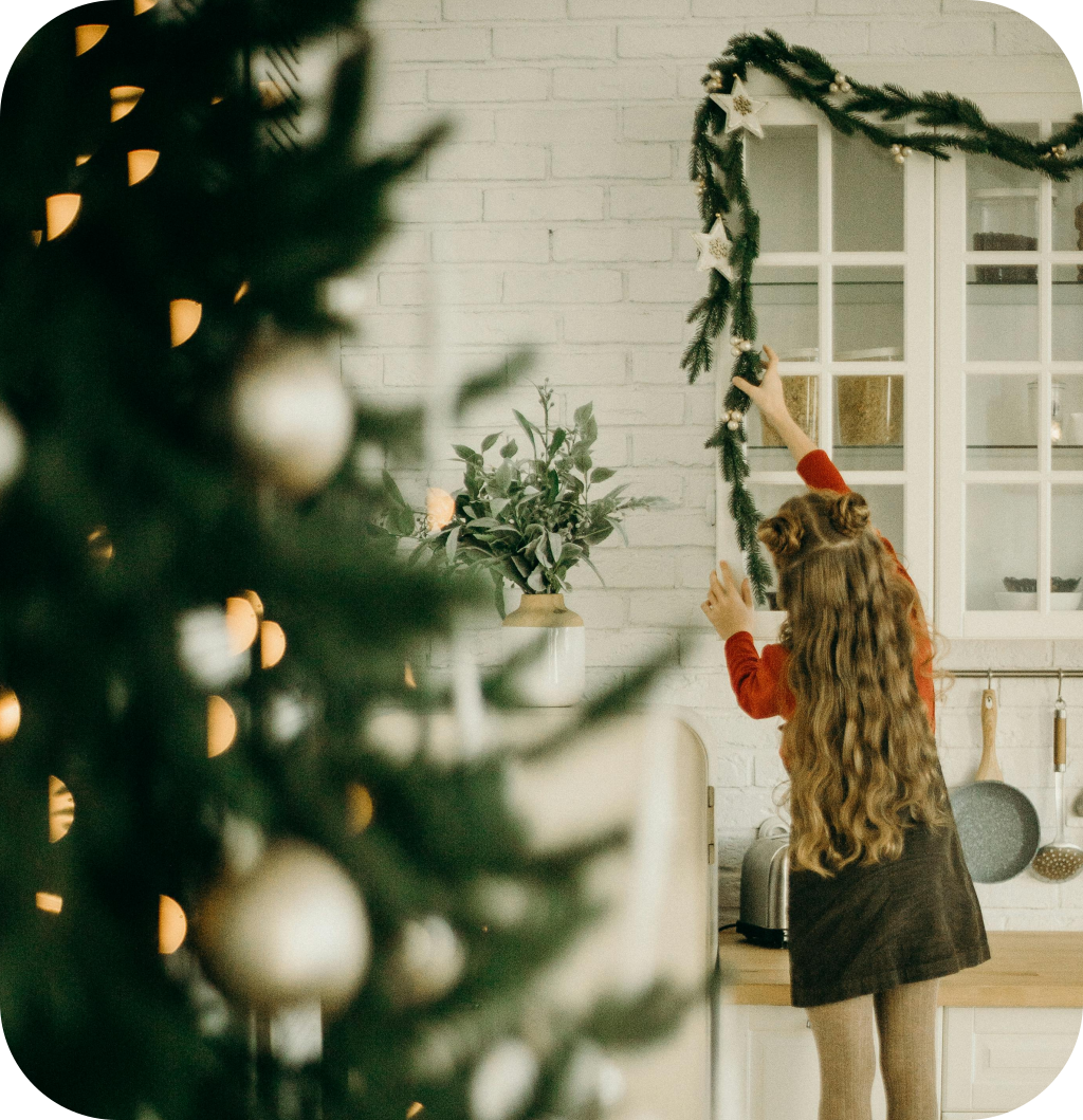 A child placing a pine garland on top of a kitchen cabinet.