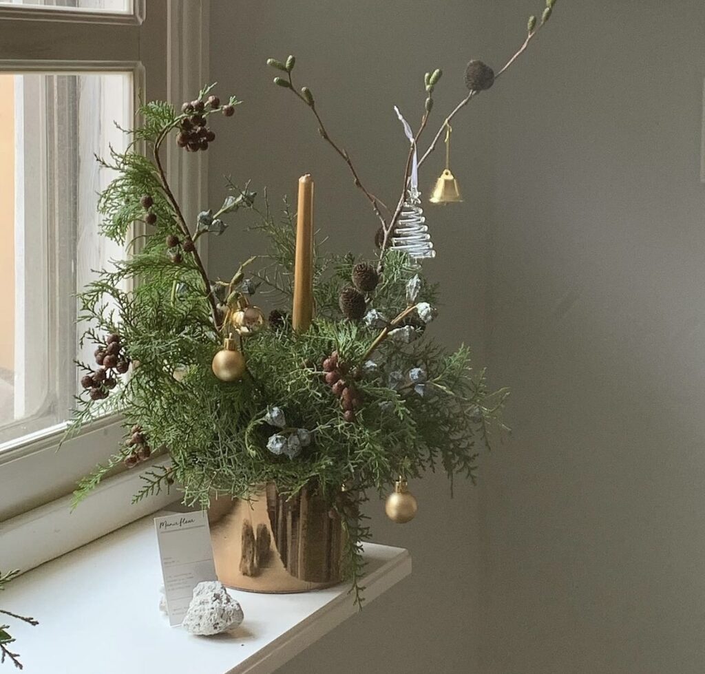 A Christmas centerpiece with gold taper candles and pine branches.