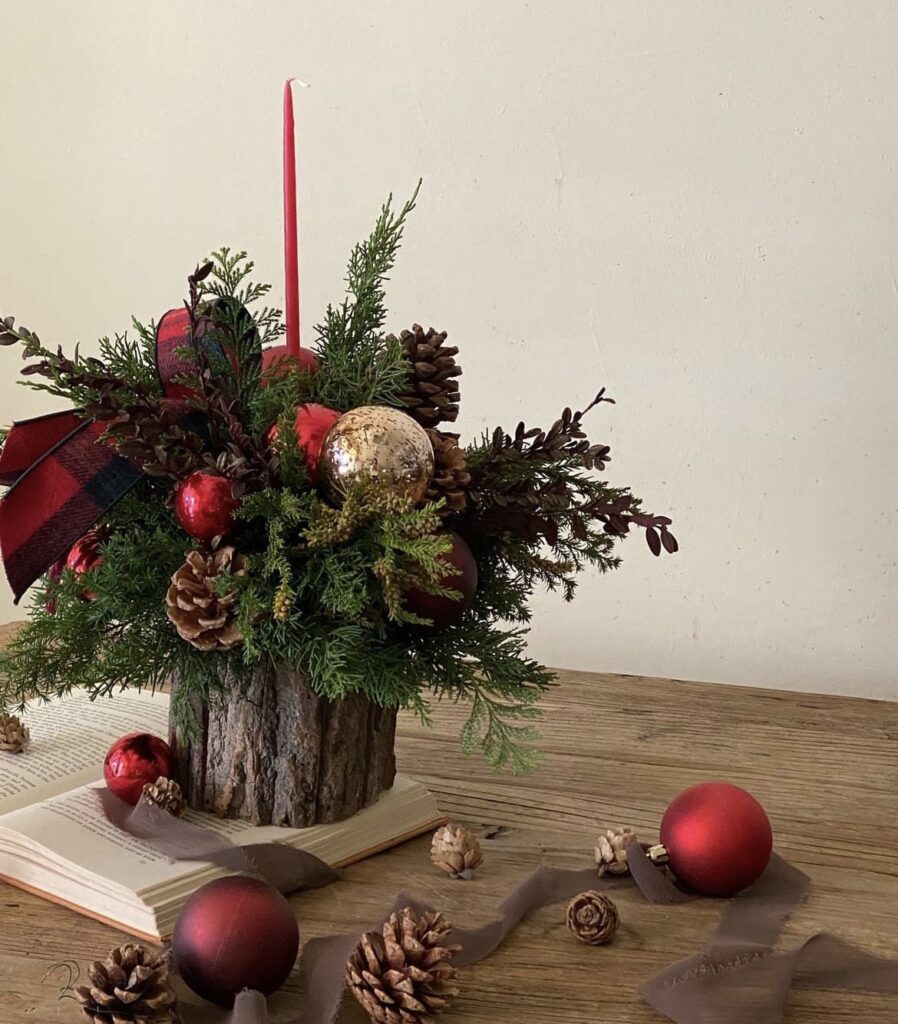 A Christmas centerpiece with a wooden log and red ornaments.