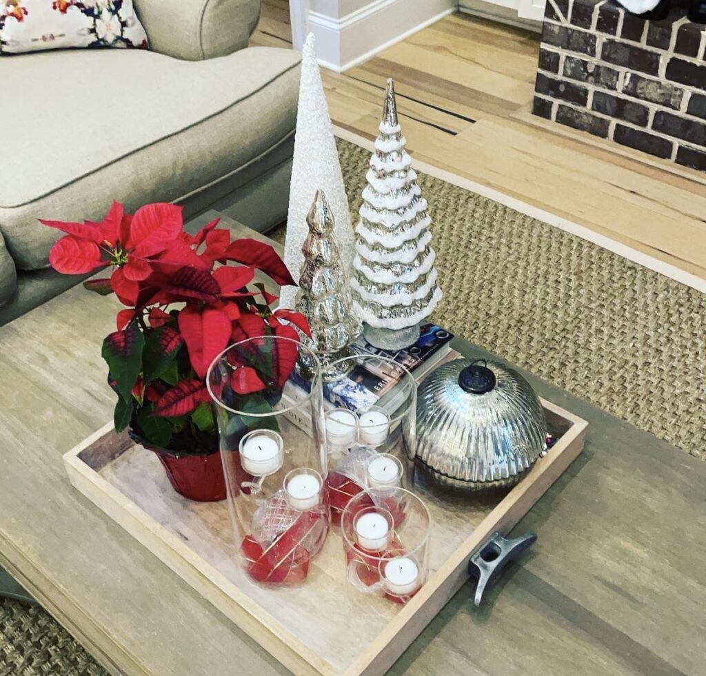 A red poinsettia with white pine trees and candles on a wooden tray.