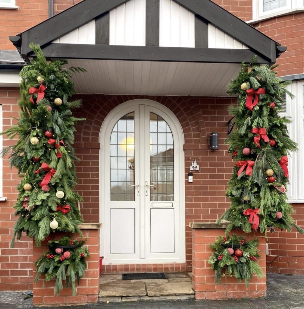 A pine branch garland with Christmas balls and red ribbon bows.