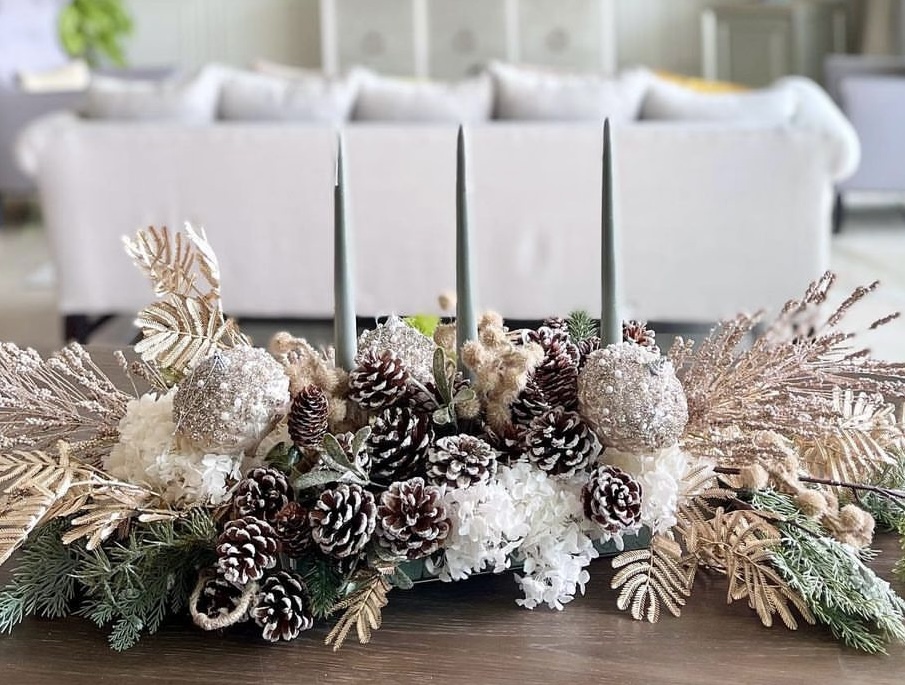 A Christmas centerpiece with pastel blue taper candles and cream leaves.