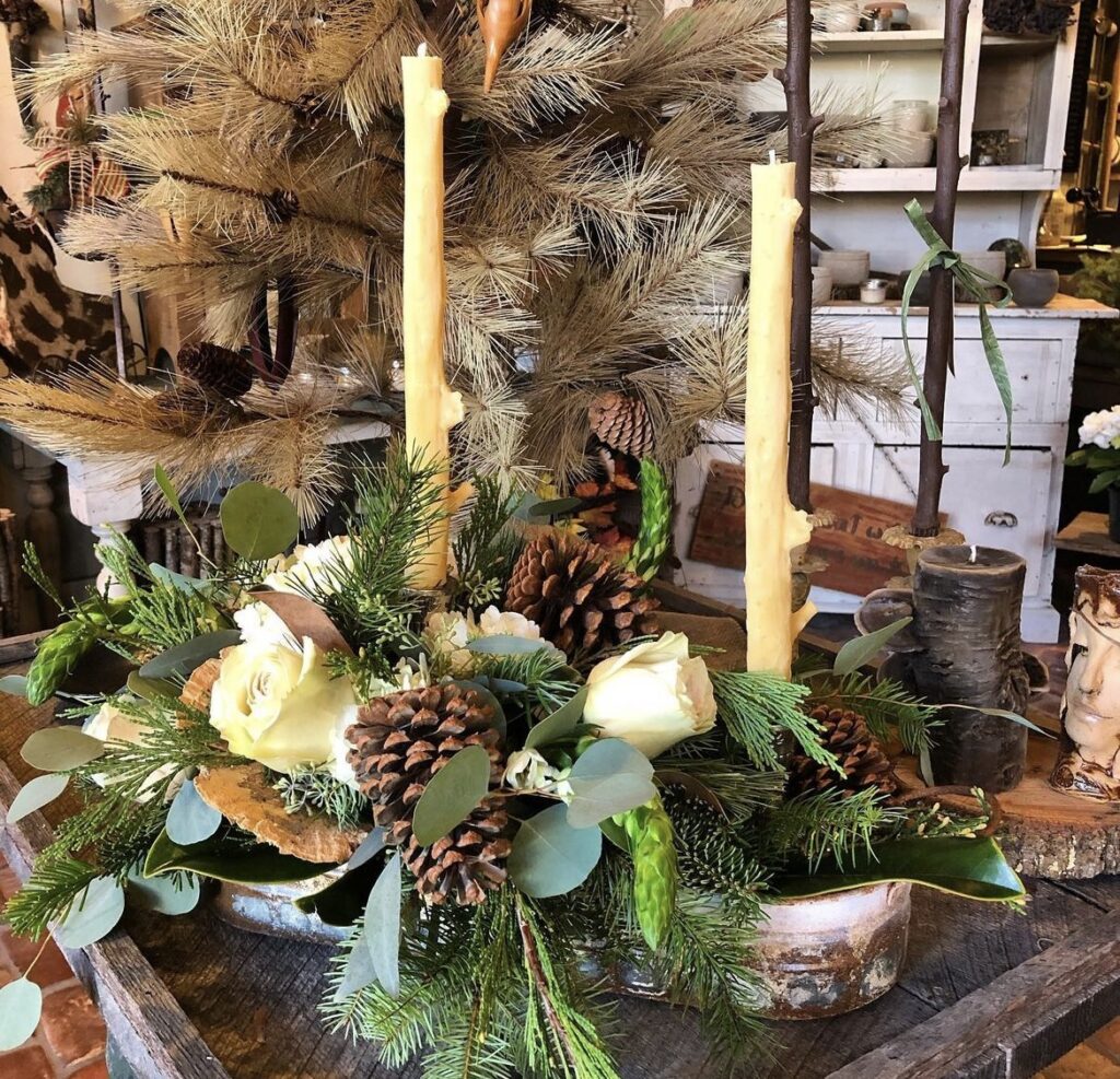 A Christmas centerpiece with pale yellow taper candles and roses.