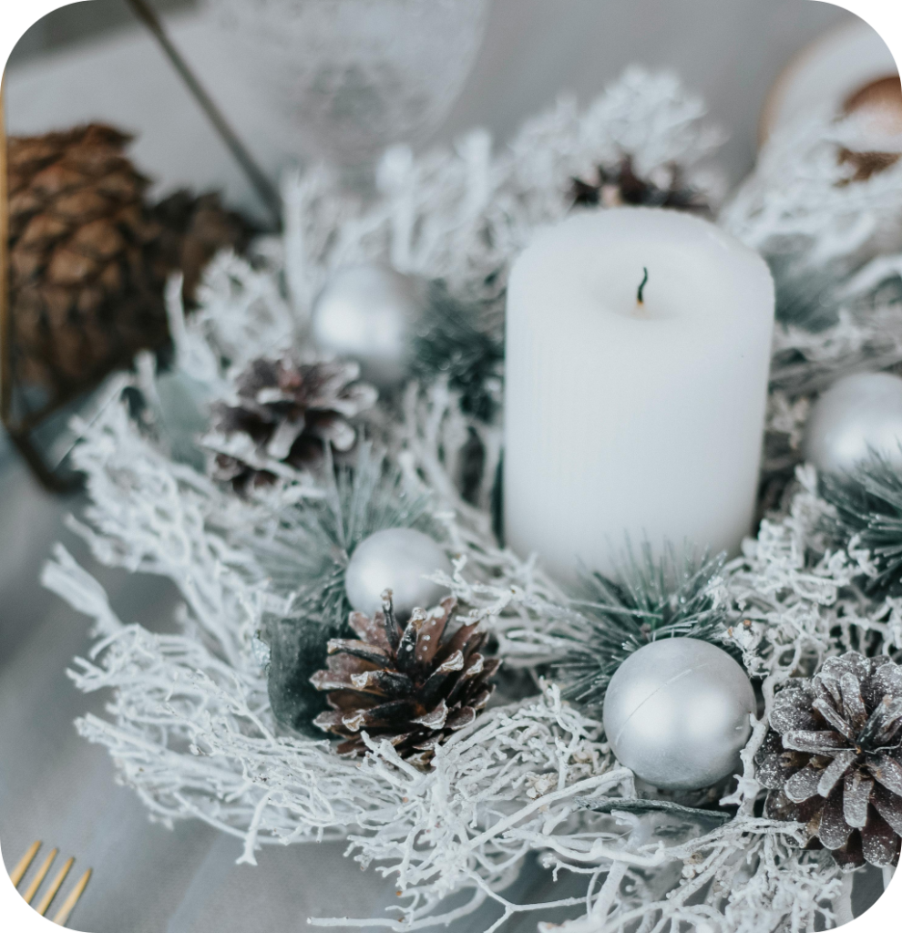 A Christmas centerpiece with a white candle, pine cones, white balls and snowy pine branches.