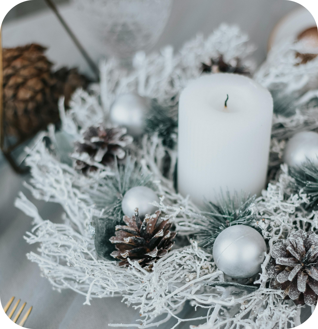 A Christmas centerpiece with a white candle, pine cones, white balls and snowy pine branches.