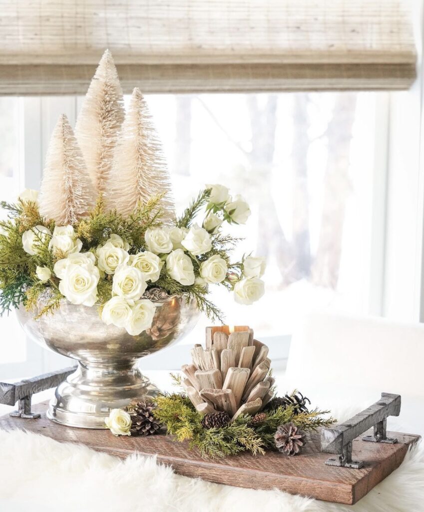 A silver vase with white flowers and pine trees.