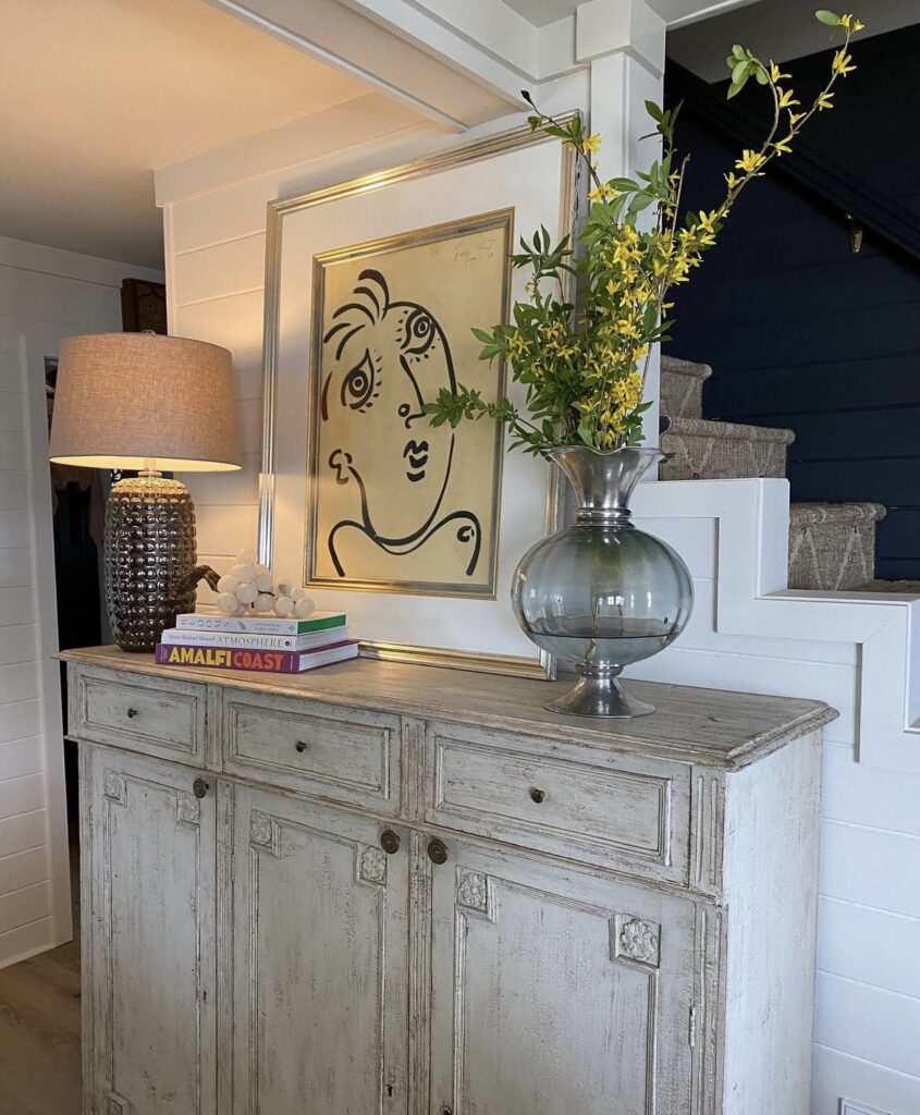 A white distressed console table with modern decorative items.