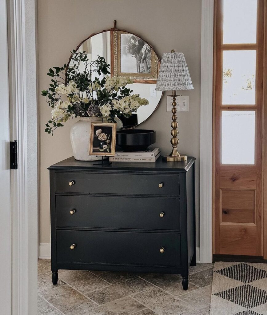 An entryway with a black console table, flowers and a lamp.