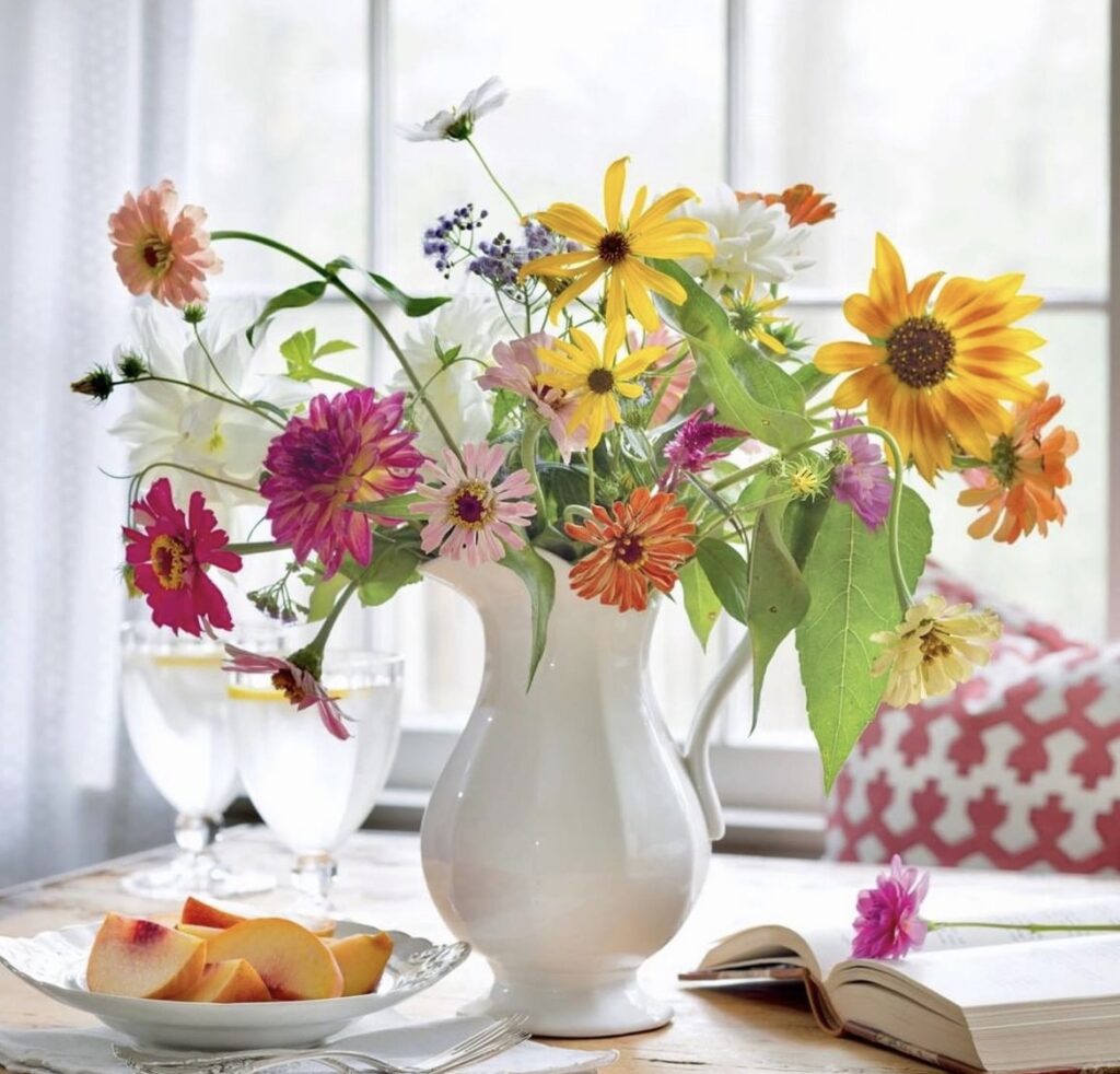 A white pitcher vase with colorful flowers.