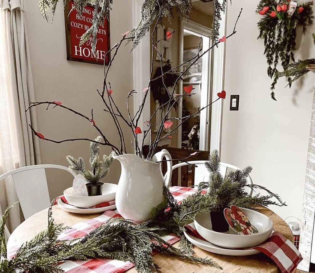 A table with red gingham napkins and table runner with pine branches, willow branches and heart ornaments.