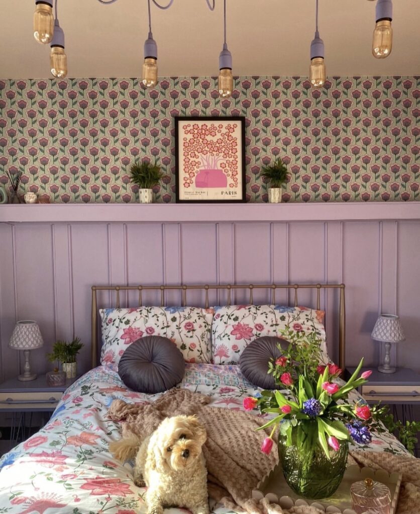 A purple bedroom with fresh flowers and floral bedding.