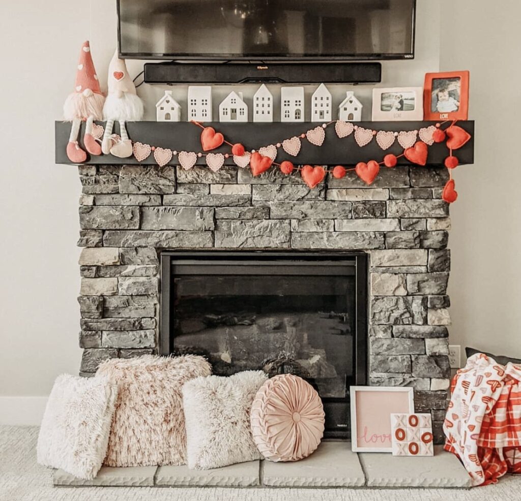 A mantel with Valentine garlands, pink pillows, and white houses.