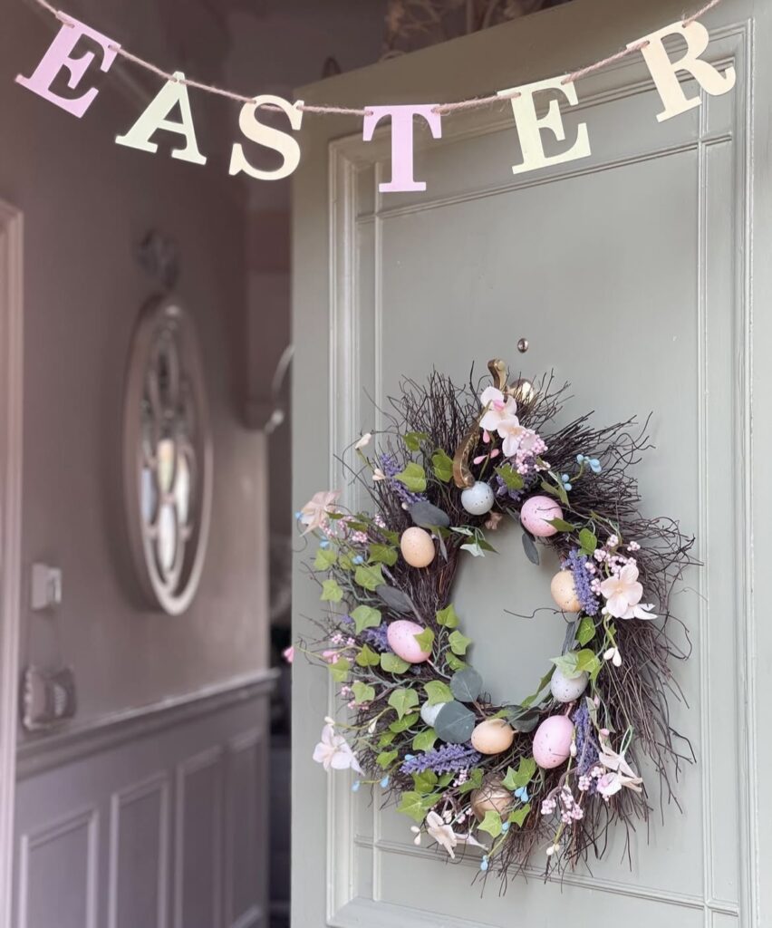 A wreath with Easter eggs and an Easter garland above a green front door.