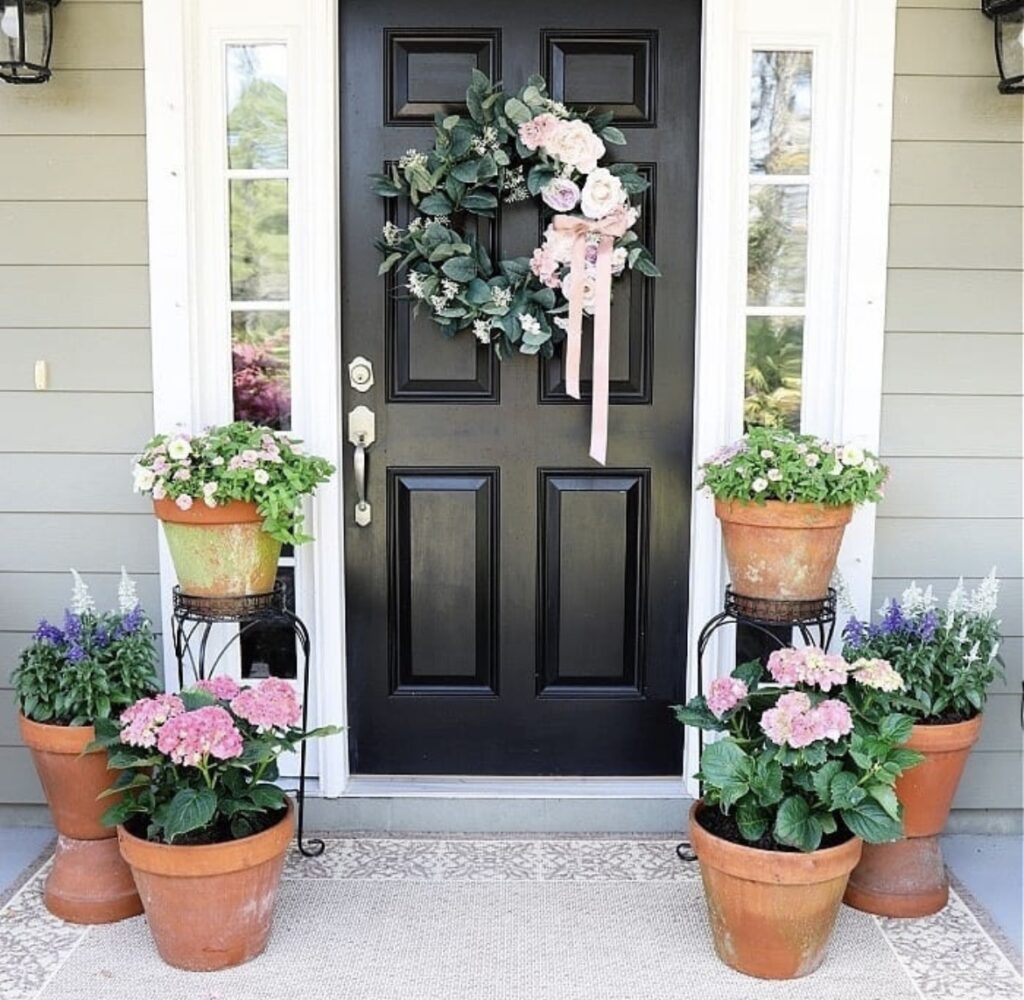 A wreath with greenery and a pink ribbon bow on a black front door.