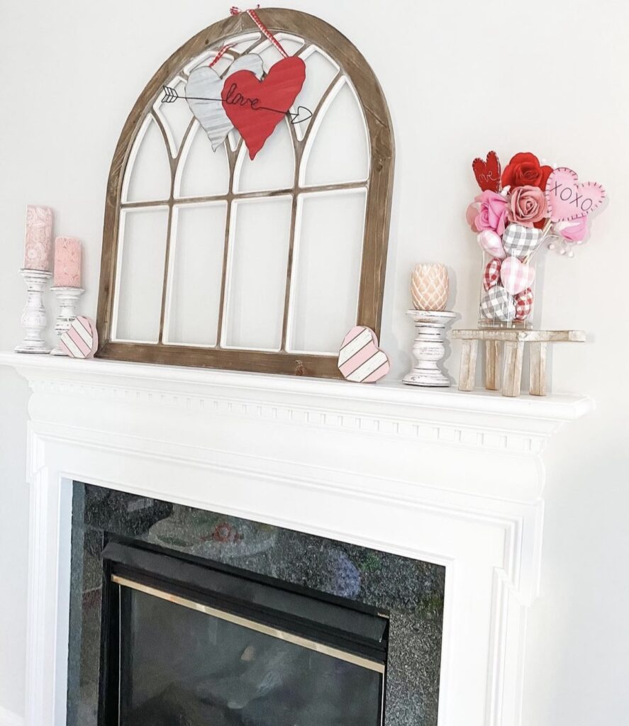 A Valentine mantel with distressed candle holders, pink candles, hearts, and flowers.