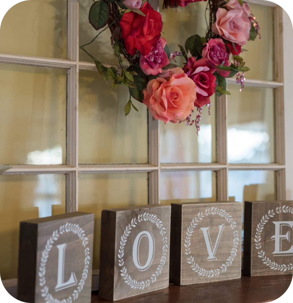 A mantel with a love sign and a floral wreath.