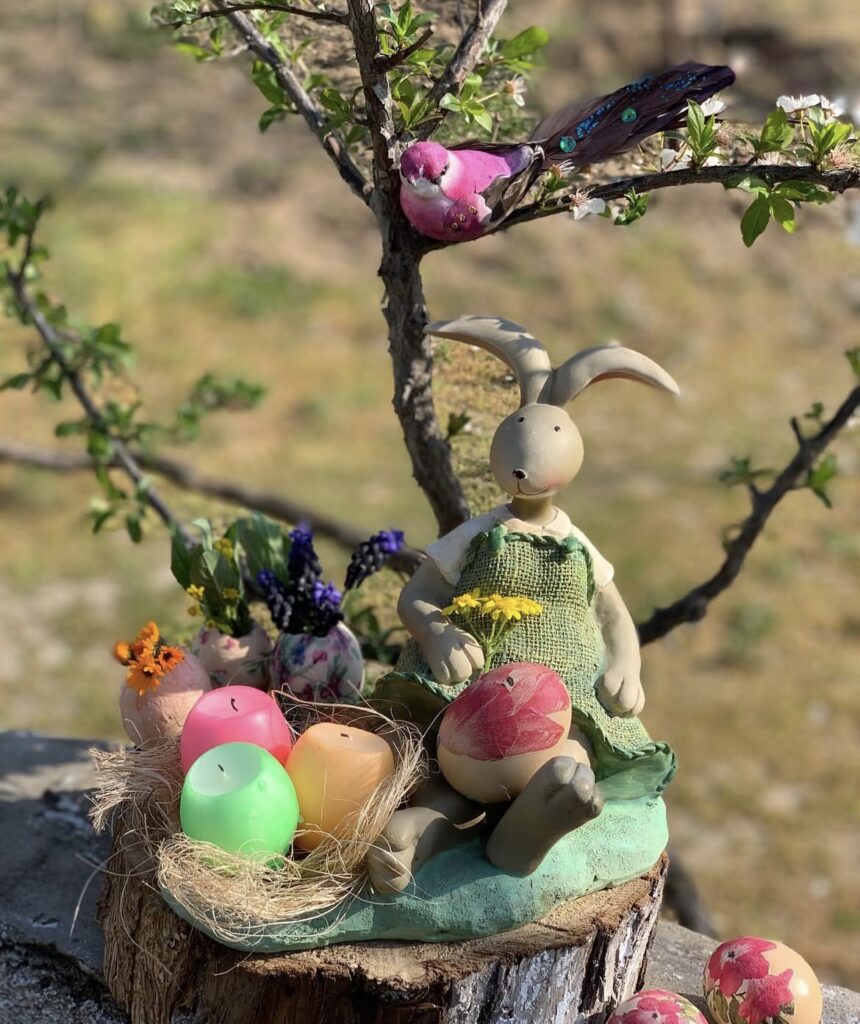 Easter eggs, candles, and a rabbit figurine in a garden.