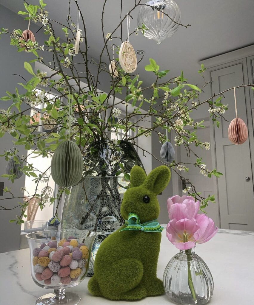 A moss rabbit figurine with branches and Easter eggs.