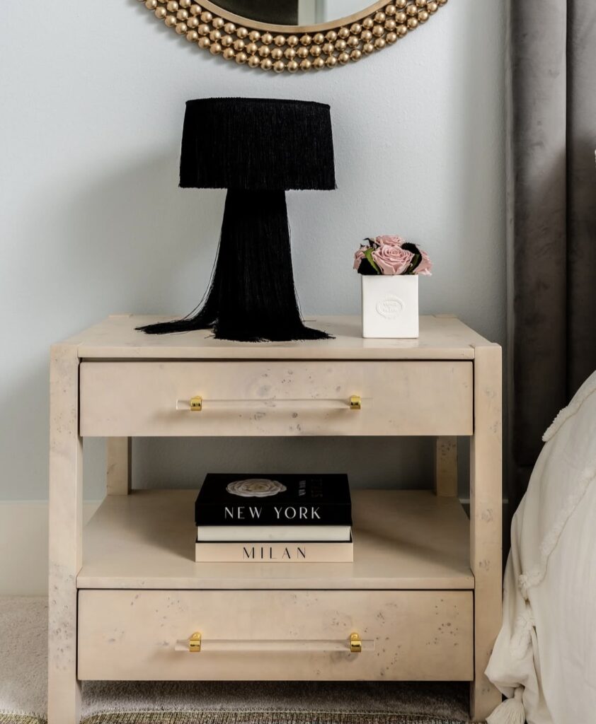 A black fringe lamp on a wooden nightstand in a modern bedroom.
