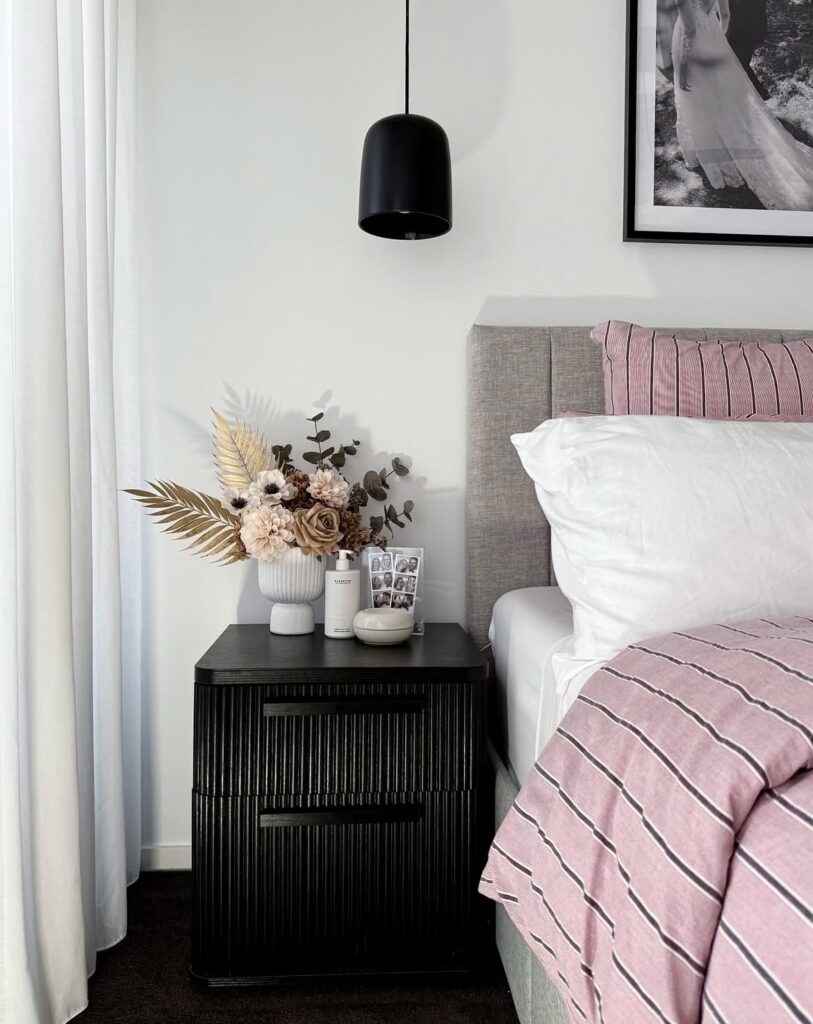 A black nightstand with a dried floral arrangement.