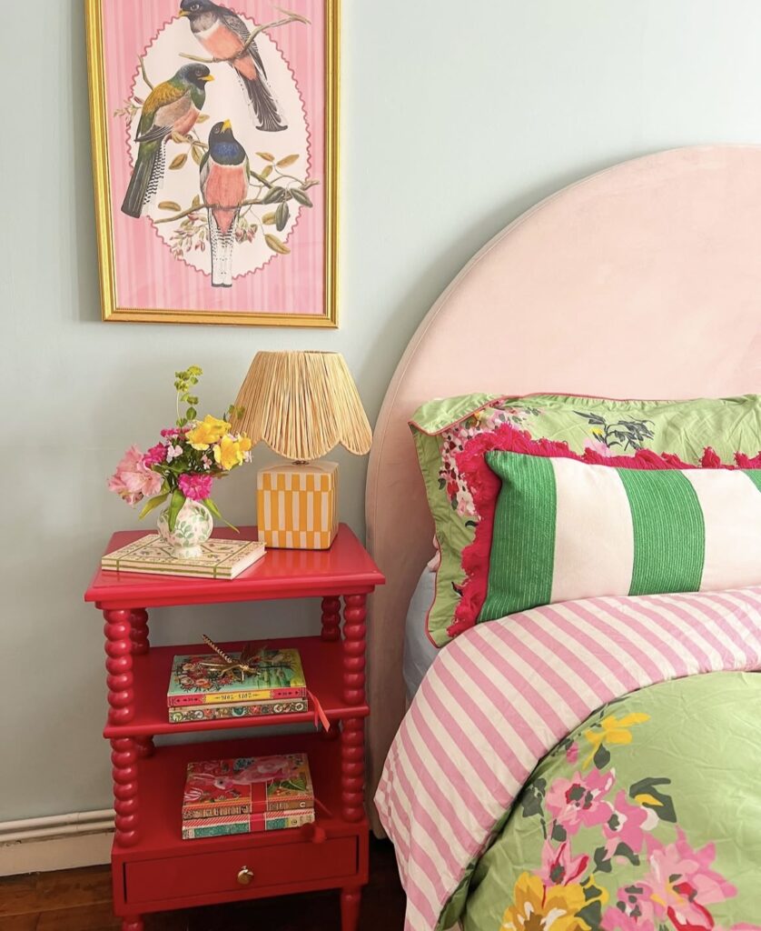 A red nightstand with colorful books and a yellow lamp.