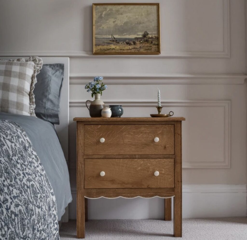 A vintage nightstand with a bronze candlestick holder and a vintage painting.