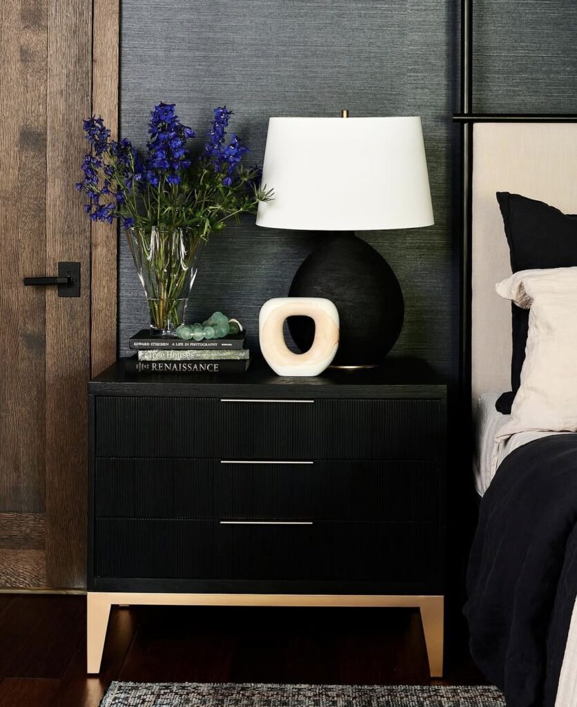 A black nightstand with a black lamp and a geometric vase.
