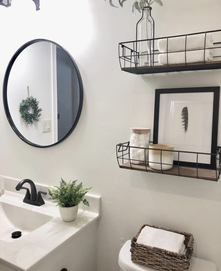 A modern bathroom with black wall mounted shelves and a woven storage basket filled with toilet paper.