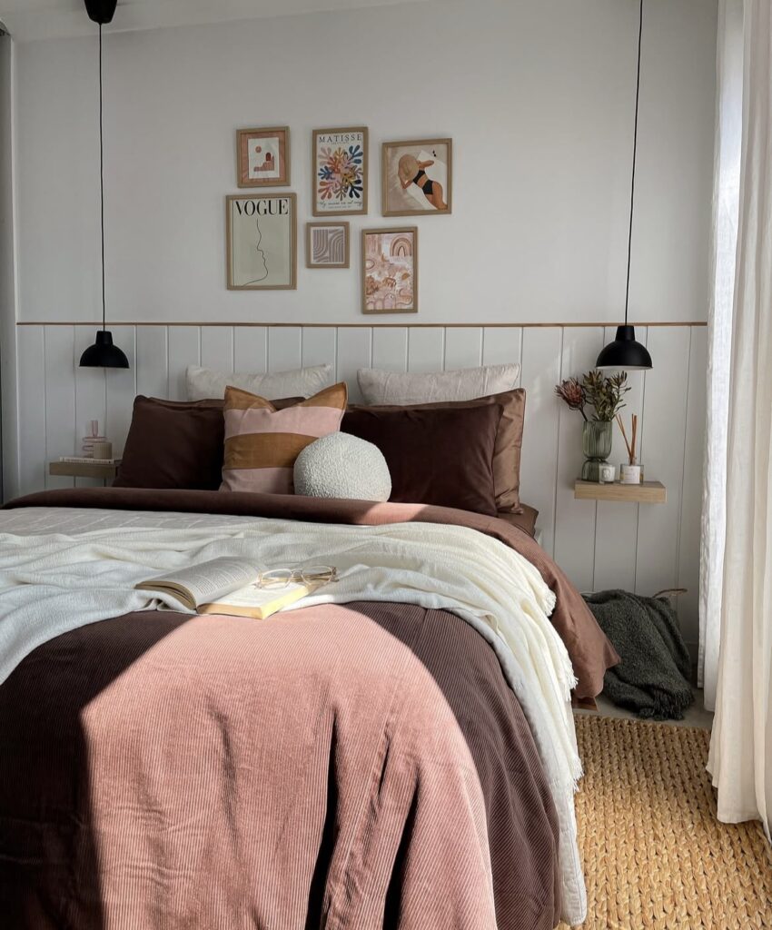 A bedroom with a gallery wall with muted pink and burgundy shades.