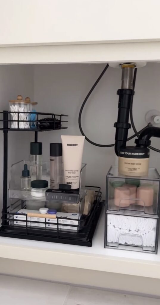 A black under the sink organizer filled with bathroom products.