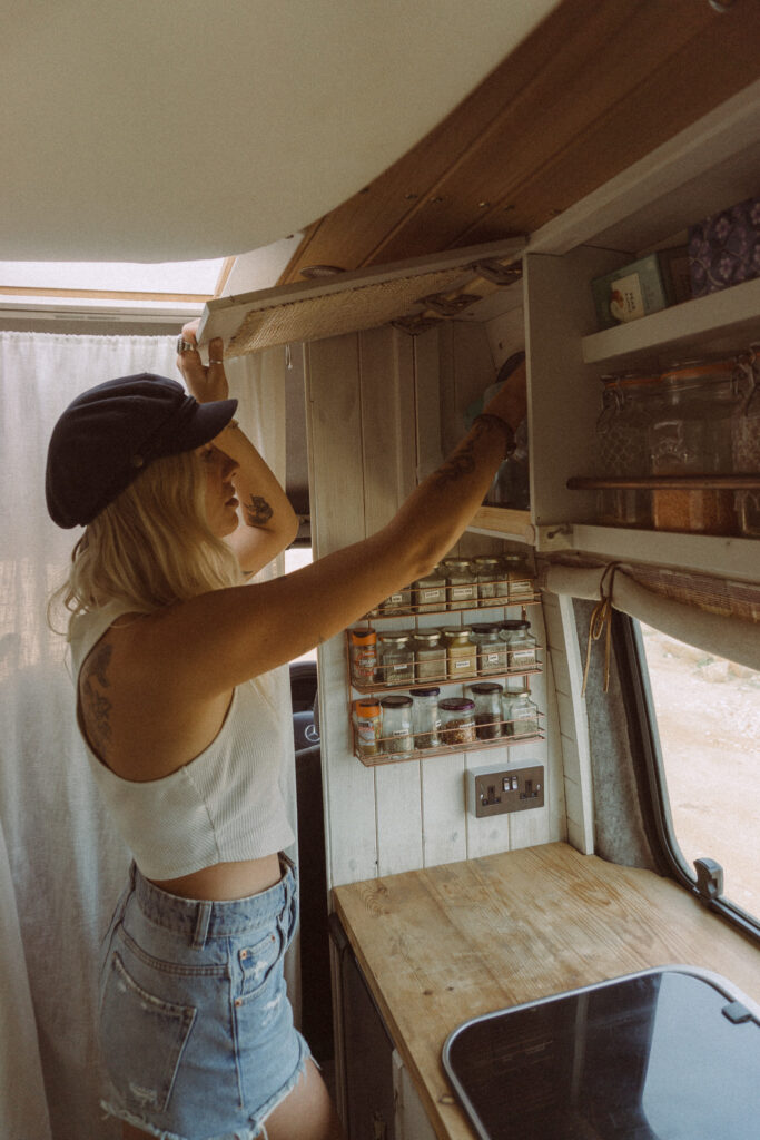 A woman taking something in a kitchen cabinet.