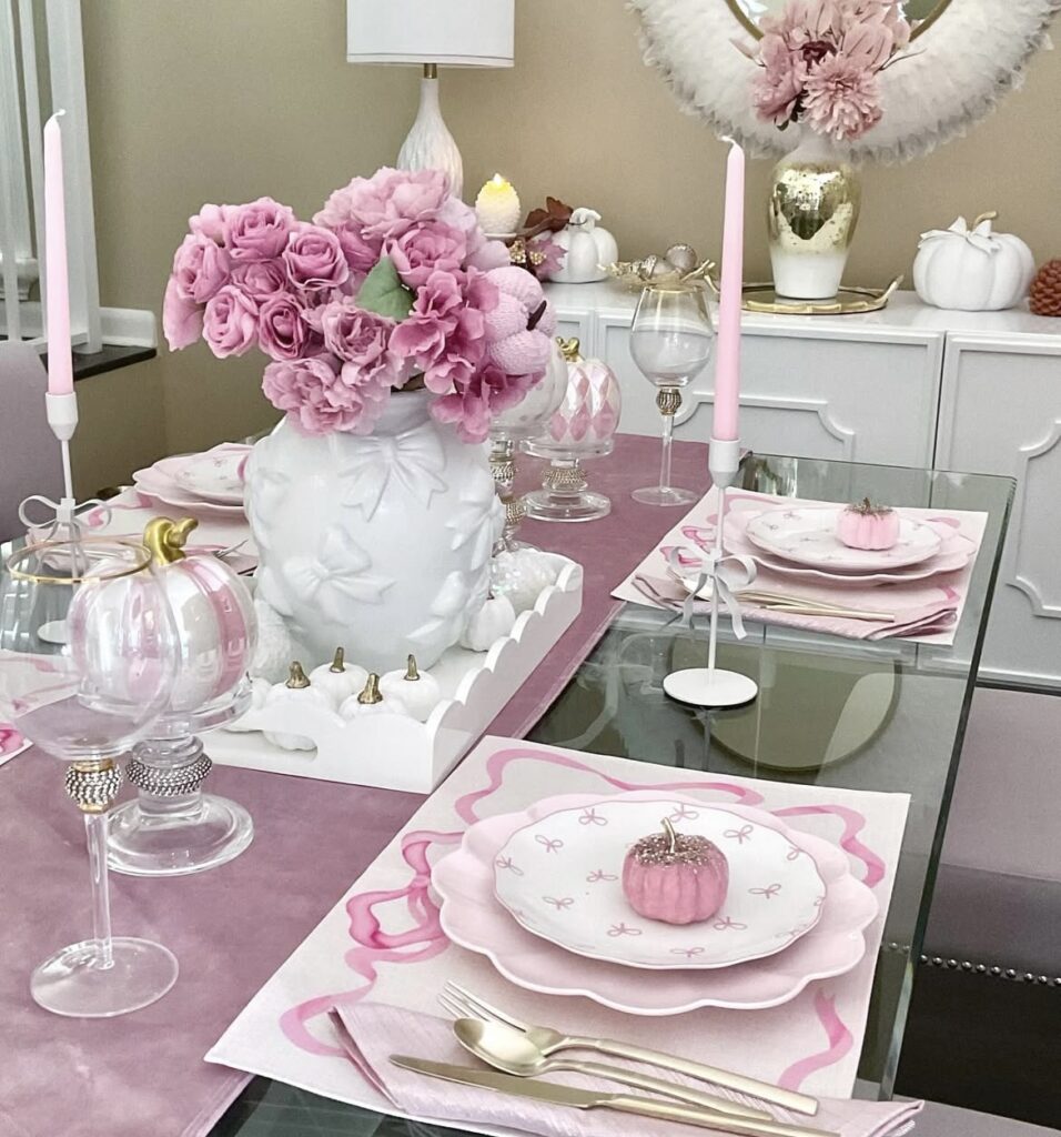 A dining table with a pink table runner and pink pumpkins.