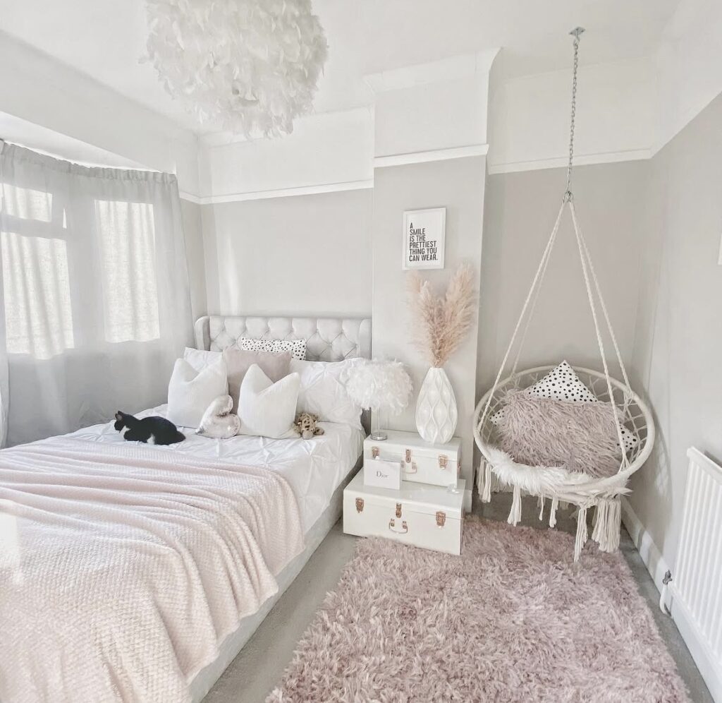A white bedroom with a light pink rug, blanket, and swing chair.