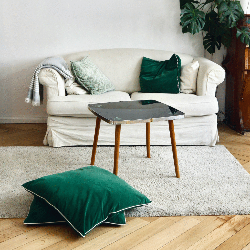 A white sofa with forest green throw pillows.