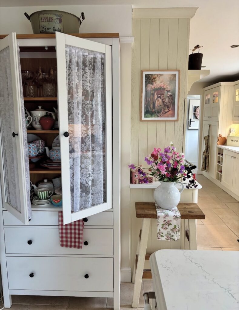A white kitchen cabinet with floral accessories.