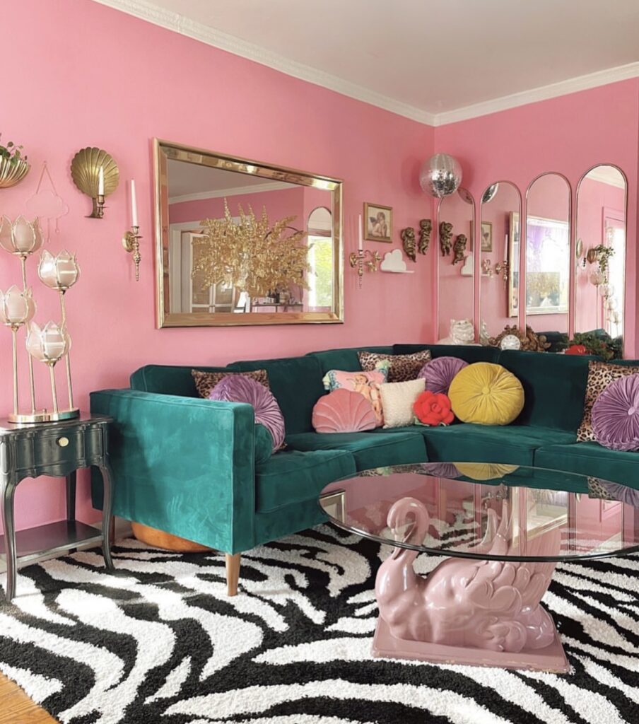 An eclectic living room with a green sofa, pink walls, a zebra rug, a pink swan coffee table and antique mirrors.