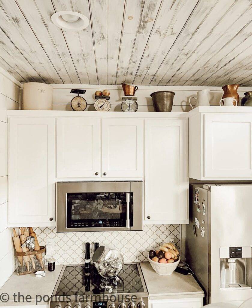 A white kitchen cabinet with antique pitchers above it.