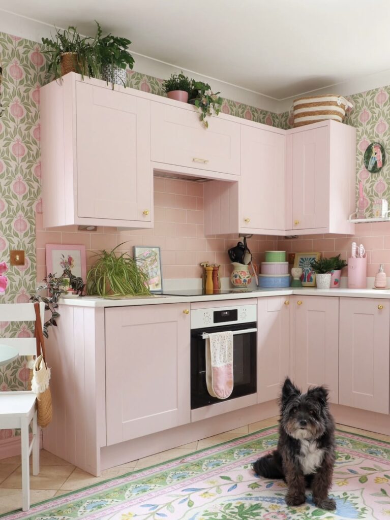 A pink kitchen with floral wallpaper and rug.