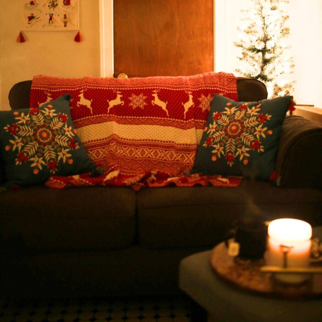 A Christmas living room with cozy pillows and a blanket.