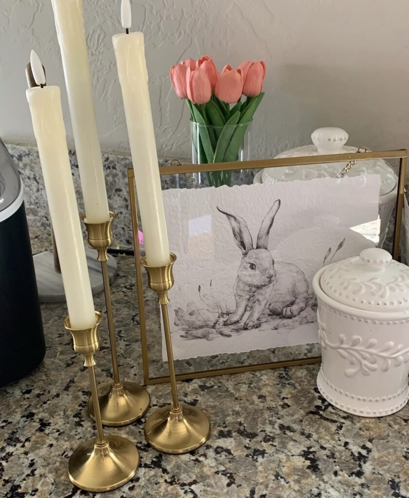 A vintage bunny art print with gold candle holders.