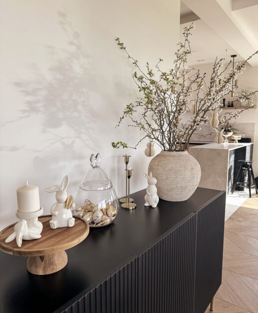 A bige ceramic vase with branches, white bunny figurines and gold Easter eggs.