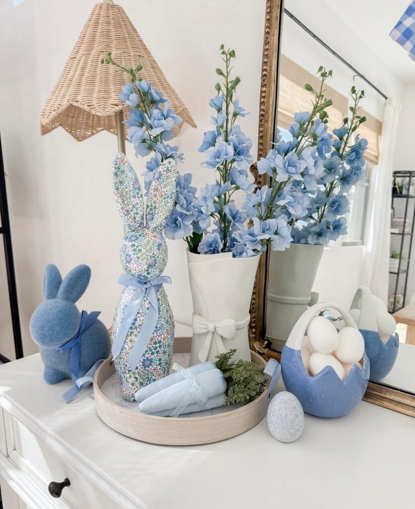 A beige tray with blue carrots, a blue bunny figurine, and a white vase filled with blue flowers.